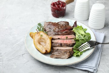 Delicious roasted beef meat, caramelized pear and greens served on light textured table