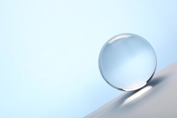 Transparent glass ball on table against light blue background. Space for text