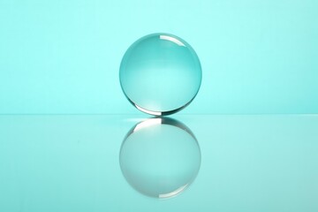 Transparent glass ball on mirror surface against turquoise background