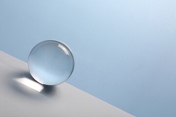 Transparent glass ball on table against light blue background. Space for text