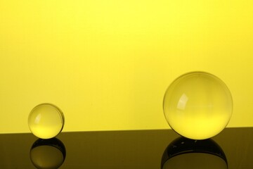 Transparent glass balls on mirror surface against yellow background. Space for text