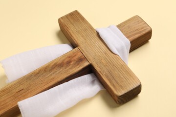 Wooden cross and white cloth on beige background, closeup. Easter attributes