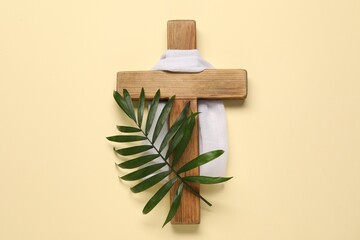 Wooden cross, white cloth and palm leaf on beige background, top view. Easter attributes