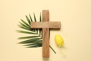 Wooden cross, painted Easter egg and palm leaf on beige background, top view
