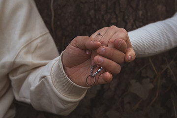 Dos manos con anillos de boda se abrazan suavemente y muestran un collar con un anillo adicional,...