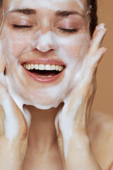 smiling young female with foaming face wash washing face