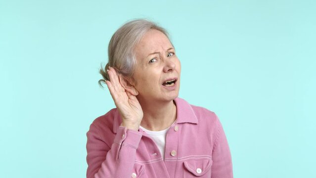 This video captures a curious senior woman in a pink jacket, placing her hand to her ear in a classic eavesdropping pose, her focused expression suggesting she's keenly listening in on a conversation.