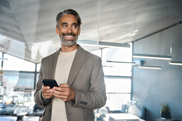 Happy middle aged business man executive using mobile cell phone in office looking away at copy...
