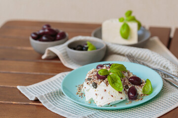 Feta cheese sliced on blue plate with sesame, flax seeds, served with black olives and basil leaves. Delicious and healthy breakfast on terrace