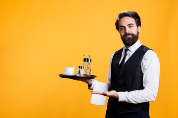 Waiter employee presenting ad aside and carrying restaurant tray, working as luxurious personnel to serve clients. Young man with formal attire creating advertisement pointing to sides.