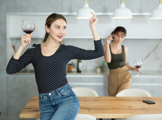 Relaxed middle-aged woman delightfully dancing and drinking wine in goblet in her house