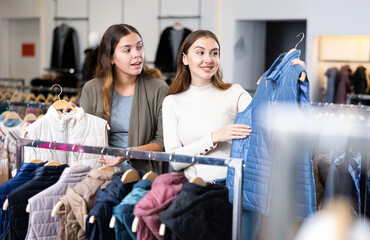 Joyful young women choosing between white and blue waistcoats in a clothing store