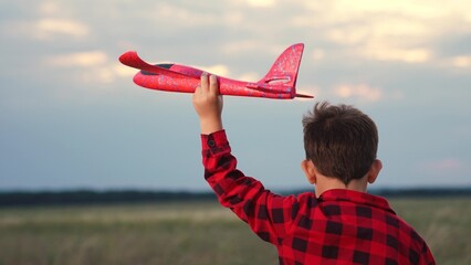Cheerful male kid running with red airplane toy imagine pilot flight at summer field closeup back...