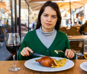 Positive female tourist tasting delicious appetizing roasted suckling pig Toston asado with side...