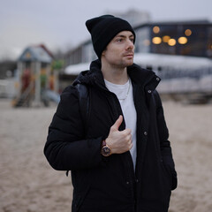 Young man in black winter jacket and hat on the beach - 739581224