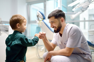 Friendly dentist greets cute toddler boy in office. Doctor encouraging with small child patient and giving him "high five". Kids doc establishes contact with little patient