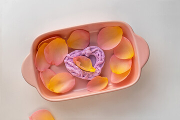 Bar of soap and rose petals in pink soap dish. Pastel colors, flat lay. Bar of soap in shape of...