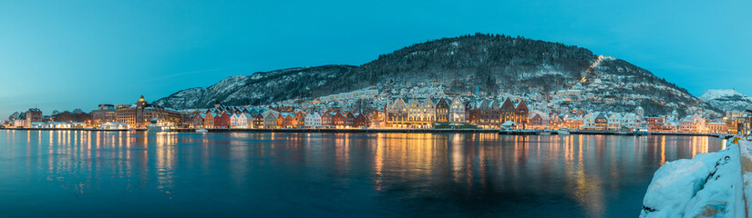 Fototapeta premium Beautiful evening panorama of Bergen waterfront, Bryggen area. Magical wide cityscape at night, covering the whole bay of Bergen. Long exposure, lights on houses are lit.