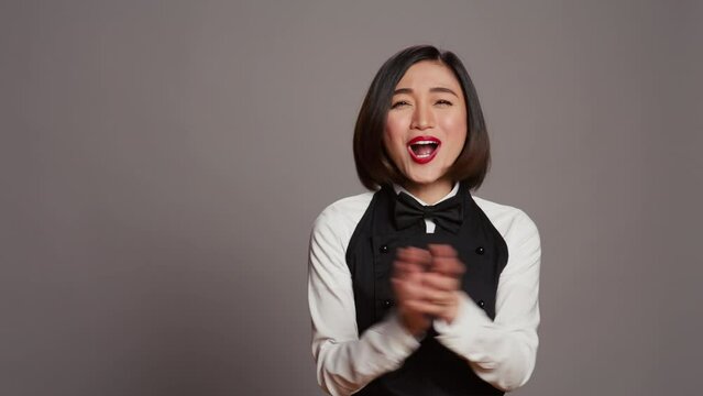 Asian server applauding someone and cheering for success, saying congratulations in front of camera. Waitress in formal uniform clapping hands, doing standing ovation gesture. Camera B.