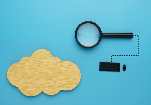 Flatlay picture of wooden cloud with magnifying glass and miniature keyboard. Cloud search engine optimization.