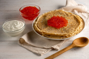Crepes, thin pancakes, Russian pancakes with red caviar on white table.