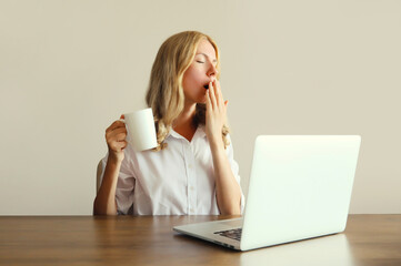 Tired overworked sleeping woman employee yawns, drinks coffee working with laptop in office