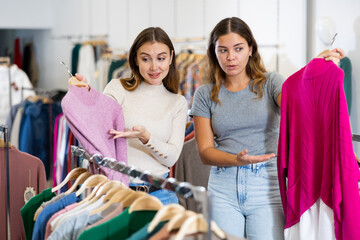 Portrait of confident female consultant helping girl choose warm knit sweater in apparel store