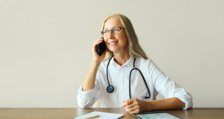 Woman doctor working calling on smartphone while sitting at desk in clinic office