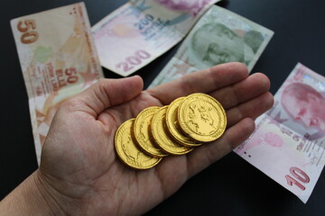 A hand holds a gold coin with the word dragon on it. Turkish banknotes in the background