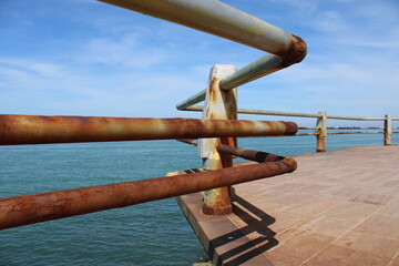 A rusty fence with a blue sea in the background.Rusty iron railing, beautiful sea and sky landscape view between rusty railing gap.