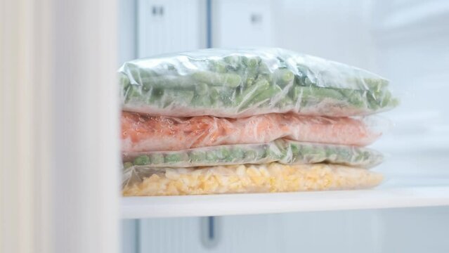 Frozen vegetables in a plastic bags in freezer close-up, front view.
