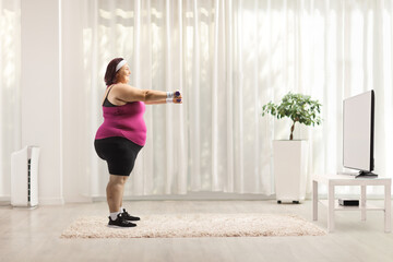 Fototapeta na wymiar Full length profile shot of a plus size woman exercising with dumbbells