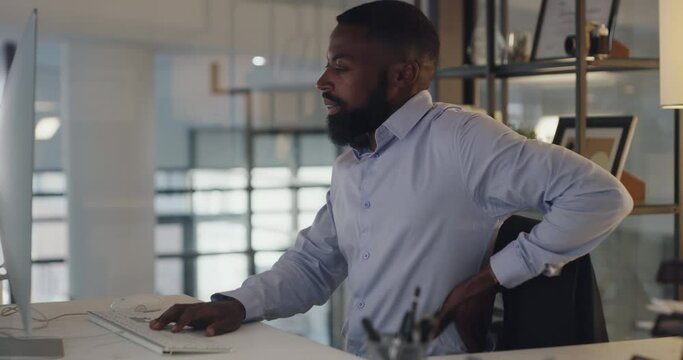 Back pain, computer and businessman for working in office, spine problem and stretching by desk. African accountant, desktop and typing in chair, muscle strain and inflammation and night at company