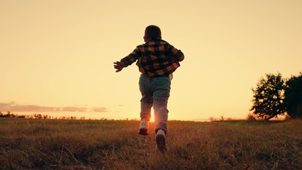 Child boy runs through green grass in sun. Childhood dream happiness concept. Happy child playing...