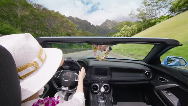 Elegant woman in lei flowers enjoying epic views. Woman travels by Oahu island 4K. Happy tourist in blue convertible car driving by H3 highway USA. Scenic Hawaii landscape seen from cabriolet open car