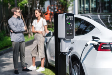 Young couple travel with EV electric car charging in green sustainable city outdoor garden in summer shows urban sustainability lifestyle by green clean rechargeable energy of electric vehicle innards - obrazy, fototapety, plakaty