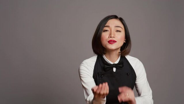 Cute flirty waitress blowing air kisses in front of camera, acting romantic with sweet gesture. Asian restaurant employee posing with a kissy facial expression, catering industry. Camera B.