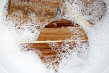 Wooden cutting board in foam of dishwashing liquid.