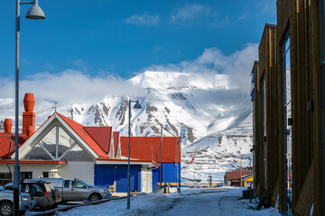 Naklejka premium 2022-05-17 A SIDE STREET IN THE TOWN OF LONGYEARBYEN WITH SNOW COVERED MOUNTAINS IN THE BACKGROUND IN SVALBARD NORWAY-