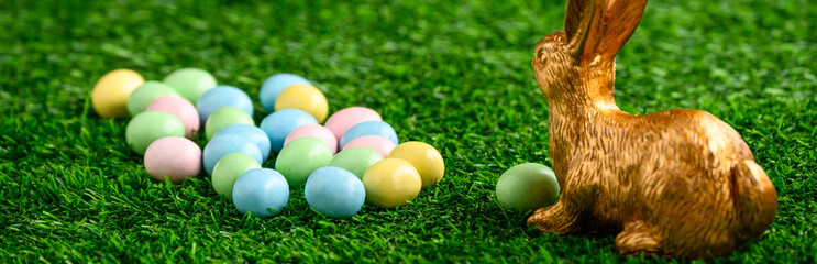 Fototapeta na wymiar Happy Easter, gold easter bunny and pastel colored candy coated Easter eggs on artificial green grass 