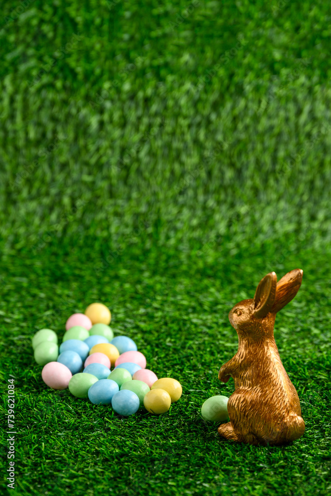 Sticker Happy Easter, gold easter bunny and pastel colored candy coated Easter eggs on artificial green grass
