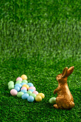 Happy Easter, gold easter bunny and pastel colored candy coated Easter eggs on artificial green grass
