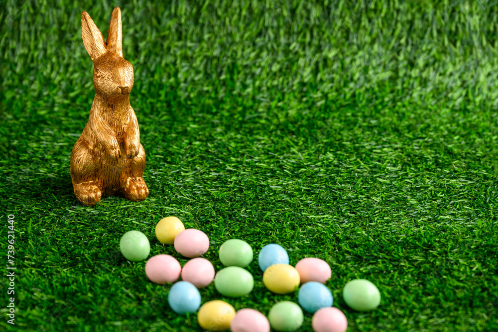 Wall mural Happy Easter, gold easter bunny and pastel colored candy coated Easter eggs on artificial green grass
