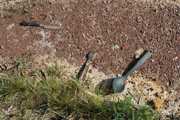 Knife, fork and spoon cutlery discarded on rocky soil ground with grass