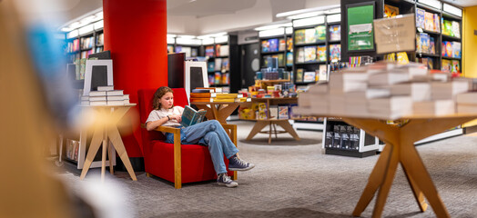 Teenage girl reading the book in large bookshop of London