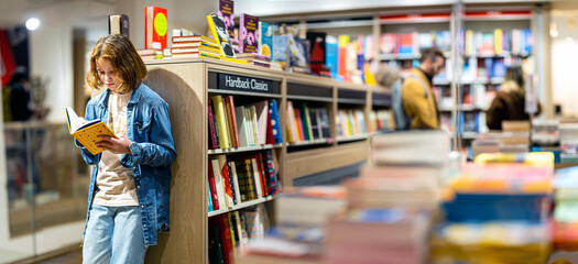 Teenage girl reading the book in large bookshop of London