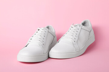 Pair of stylish white sneakers on pink background