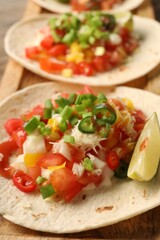 Delicious tacos with vegetables, green onion, lime and ketchup on table, closeup