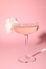 Tasty cocktail in glass decorated with cotton candy on pink background