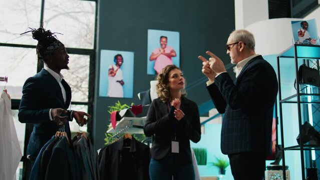 Skilled couturier asking for luxury items from store assistants, buying expensive clothing and materials for his new fashion show. Famous tailor is the patron or sponsor of the showroom. Camera B.
